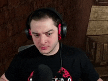 a man wearing headphones and a black t-shirt is sitting in front of a microphone .