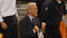 a man in a suit and tie is sitting in a stadium with his fist in the air .