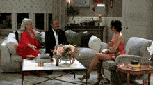 a woman in a red dress sits on a couch talking to a man in a suit