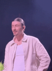a man in a white shirt and jacket is standing on a stage with his eyes closed .