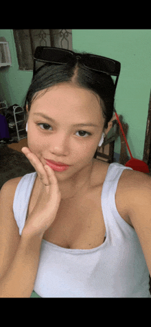 a woman wearing sunglasses and a white tank top is taking a selfie .