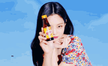 a woman in a floral dress holds up a bottle of vitamin c