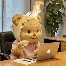 a teddy bear sitting at a desk with an apple laptop and a cup of coffee