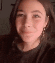 a close up of a girl wearing earrings and a black shirt making a face .