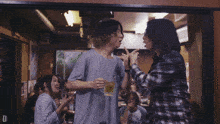 a man in a plaid shirt holds a glass of beer in a crowded room