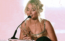 a woman is speaking into a microphone while holding an award