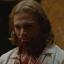 a man with blood on his face and neck looks at the camera