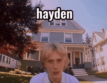 a young man stands in front of a house with the name hayden on it