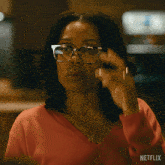 a woman in a red sweater is holding a pair of glasses in her mouth with a netflix logo behind her