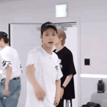 a man wearing a baseball cap and a white t-shirt is standing in a room with other people .
