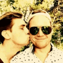 a man kissing another man on the cheek while wearing sunglasses