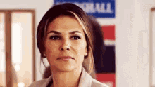 a close up of a woman 's face with a serious look on her face and a sign in the background .