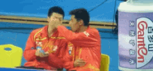 two men are sitting in front of a container of gamen