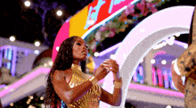 a woman in a gold dress stands in front of a neon sign that says let 's