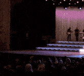 a man playing a guitar on a stage in front of a blue curtain