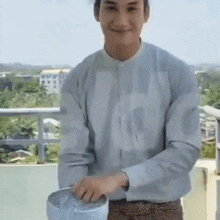 a man is standing on a balcony holding a bucket of water and smiling .