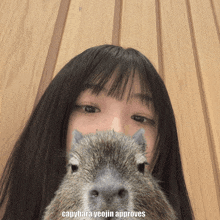 a girl is holding a capybara in front of her face