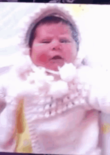 a baby wearing a white dress and a white hat is making a funny face .