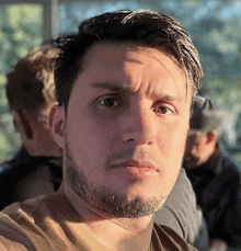 a close up of a man 's face with a beard and a brown shirt .