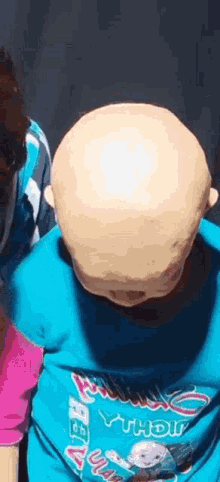 a baby with a bald head is wearing a blue shirt with a cartoon character on it .