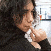 a young man with long hair is biting his thumb .