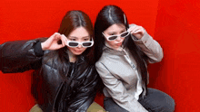 two women wearing sunglasses are sitting next to each other on a red background