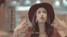 a woman wearing a red hat and earrings is making a funny face and saying `` so damn hot '' .
