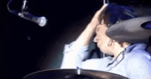 a man is playing drums in front of a microphone while holding his hand to his head .