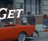 a man in a suit is running towards a red car that says get on the side