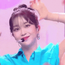 a close up of a woman wearing a blue shirt and earrings with a microphone in her mouth .