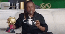a man with dreadlocks is sitting on a couch holding a skull and a cigarette .