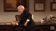 a man in a suit is dancing in front of a desk with a certificate from the university of alabama on it