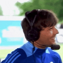 a man wearing headphones and a microphone is smiling and wearing a blue adidas jacket
