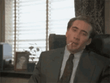 a man in a suit and tie is smoking a cigarette in front of a window .
