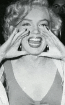 a black and white photo of a woman covering her mouth with her hands .
