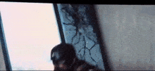 a man in a superhero costume is standing in front of a broken glass window .