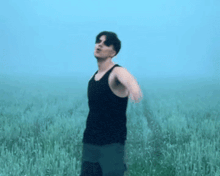 a man in a black tank top is standing in a field of grass .
