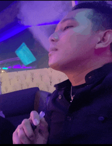 a man smoking a cigarette with a purple light behind him