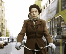 a woman in a brown coat is riding a bicycle down a city street