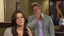 a man in a suit is covering his mouth while a woman looks on