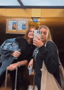 two women are taking a selfie in an elevator and one has a shirt that says i love you