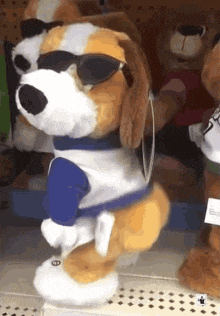 a stuffed dog wearing sunglasses and a blue shirt is standing on a shelf in a store .