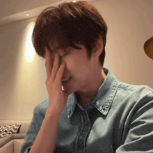 a man wearing a denim shirt covering his face with his hand