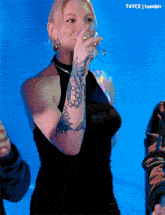 a woman with tattoos on her arm is drinking from a glass