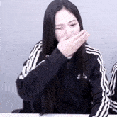 a woman wearing a black adidas jacket covers her mouth with her hand