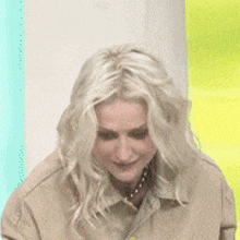 a woman with blonde hair is wearing a tan jacket and a gold necklace