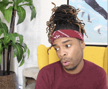 a man with dreadlocks wearing a red bandana is sitting in a chair