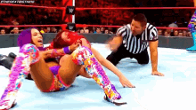 two women are wrestling in a wrestling ring while a referee looks on .