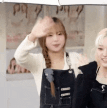 two women are standing under an umbrella and one of them is waving .
