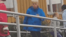 a man in a blue jacket is standing next to a white railing .